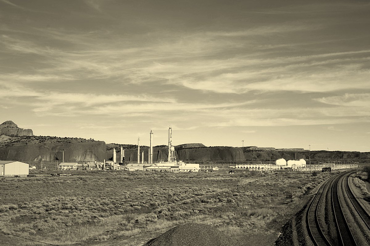 An oil refinery beside railroad tracks under red cliffs near Gallup, New Mexico