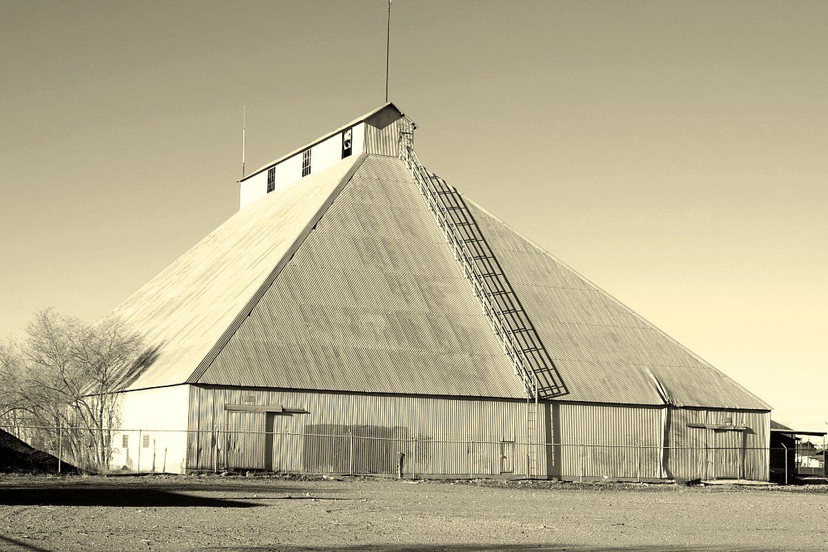 A large angular corrugated-metal grain elevator behind a fence in Las Cruces, New Mexico